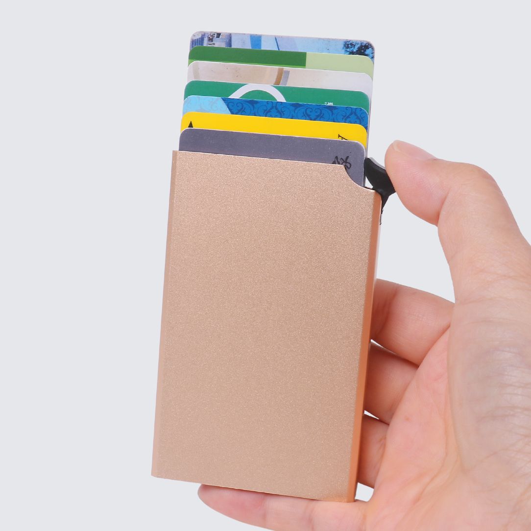 Hand holding a rose gold aluminium RFID card holder with multiple cards extended in a fan shape using a pop-up lever mechanism.
